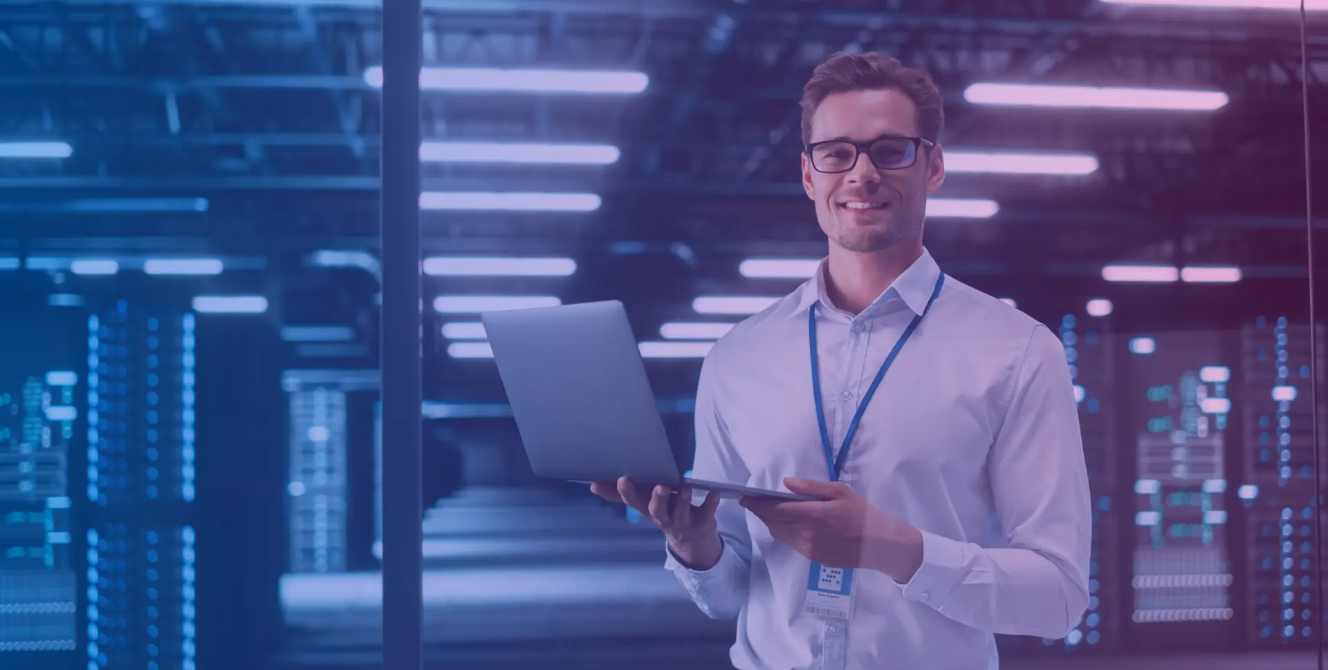 Smiling IT technician with a laptop in a server room with illuminated racks